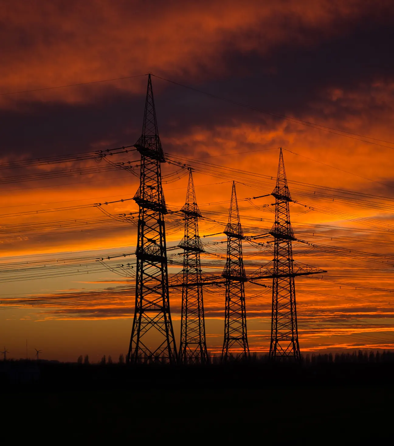 High-voltage transmission towers silhouetted against a sunset sky